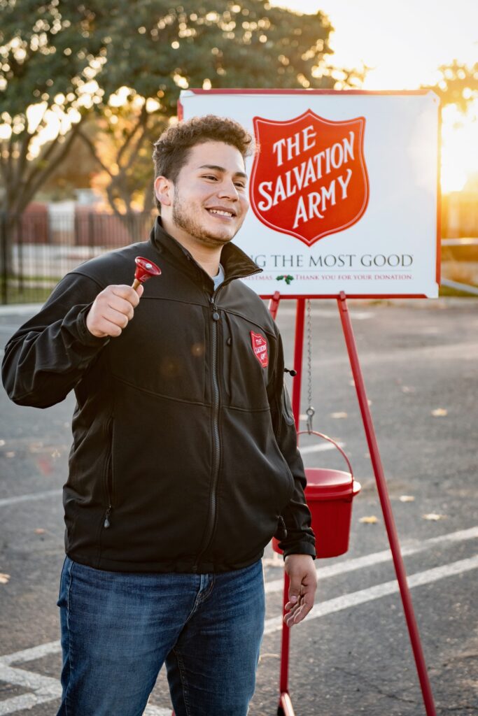 A young man ringing a bell in front of a salvation army sign